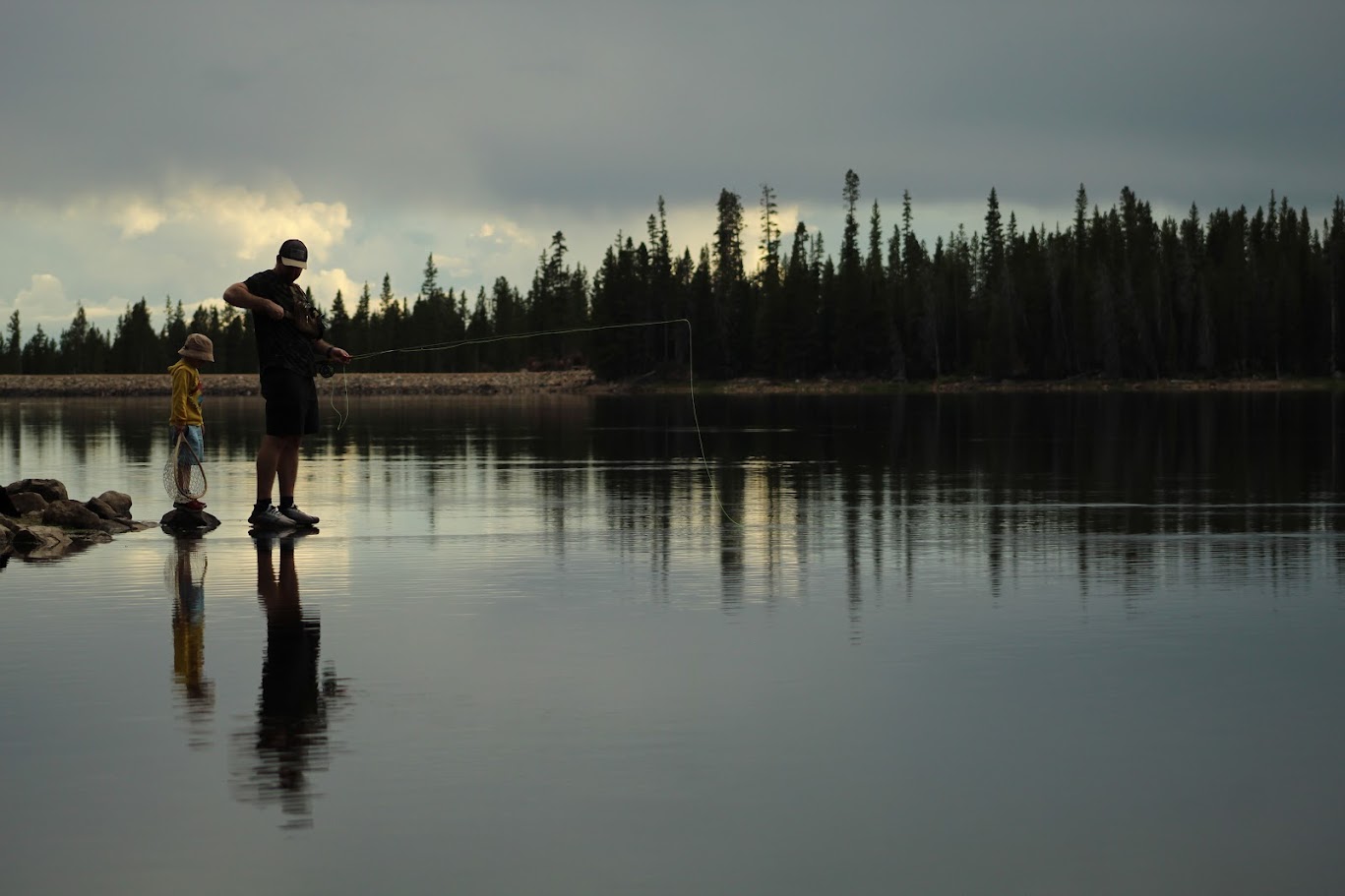 Father and child fishing together by a quiet lake at dusk.